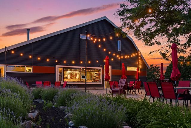 The patio under string lights at dusk, red umbrellas furled and lavender in the beds